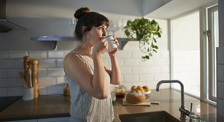A woman is drinking a cup of coffee in a kitchen.