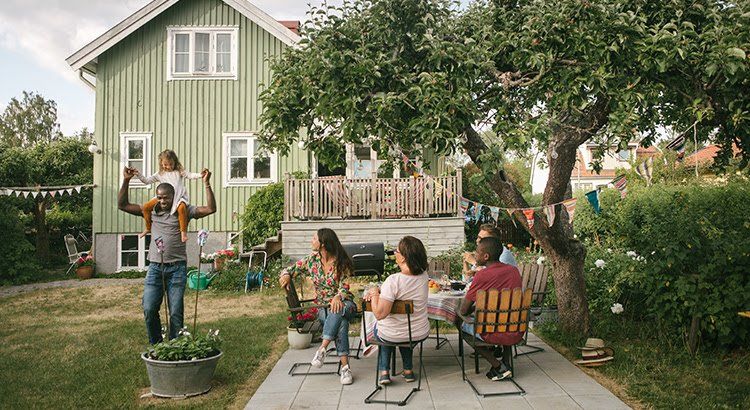A group of people are sitting at a table in front of a green house.