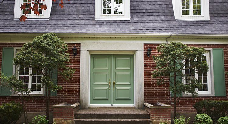 The front of a brick house with green doors and green shutters.