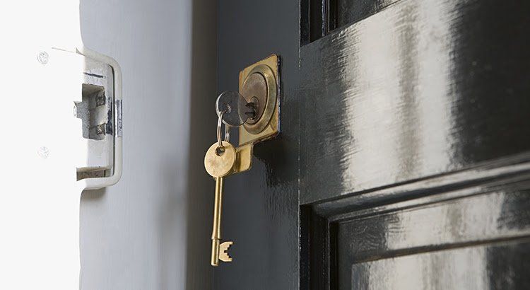 Two keys are hanging from a keyhole on a black door.