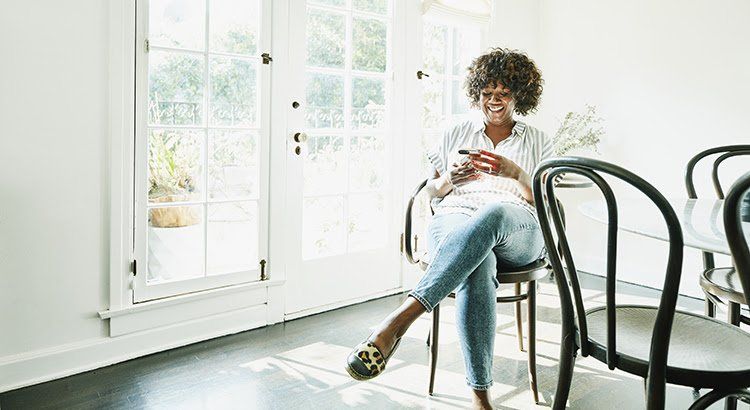 A woman is sitting on a chair in a dining room looking at her phone.