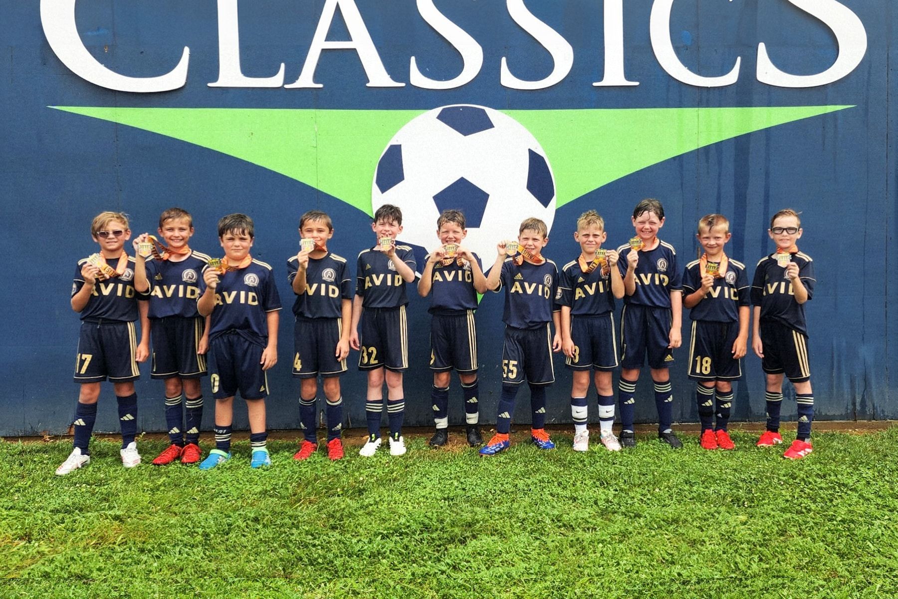 Youth soccer team posing in navy uniforms in front of a "Classics" banner and a soccer ball backdrop