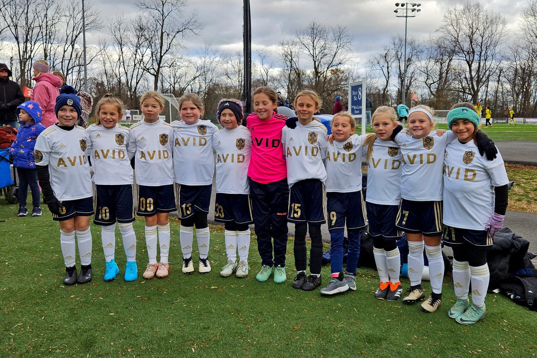 Youth soccer team posing on a field, wearing white jerseys and medals on an overcast day.