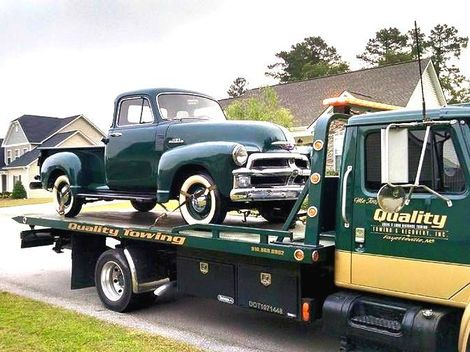 an old green truck is being towed by a quality tow truck in Fayetteville NC