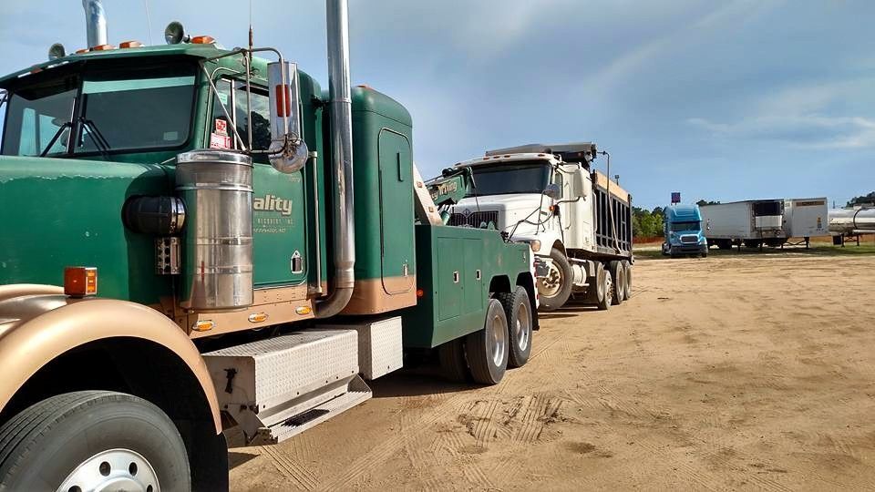 a green semi truck is parked in a dirt field .