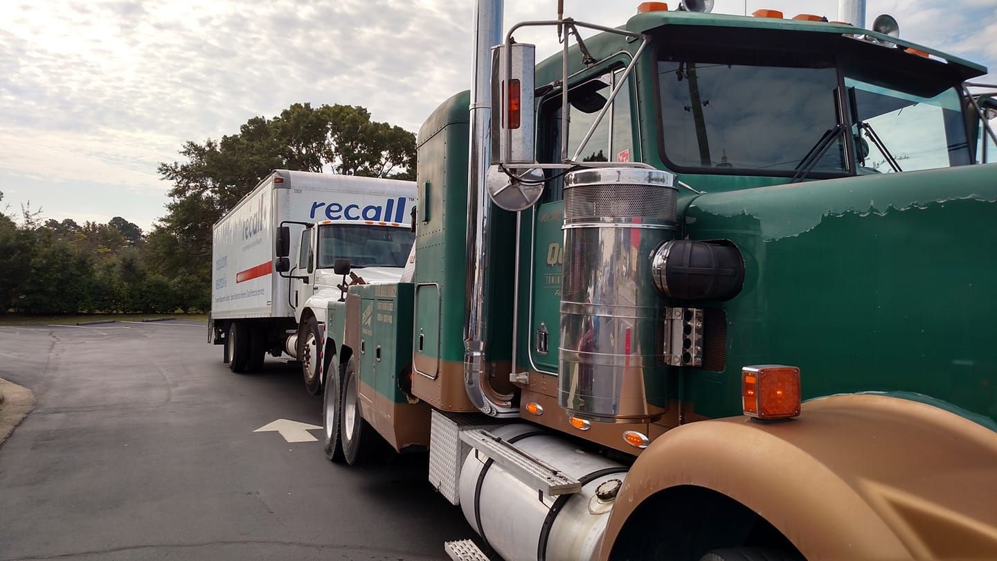 a green semi truck is parked next to a white truck .