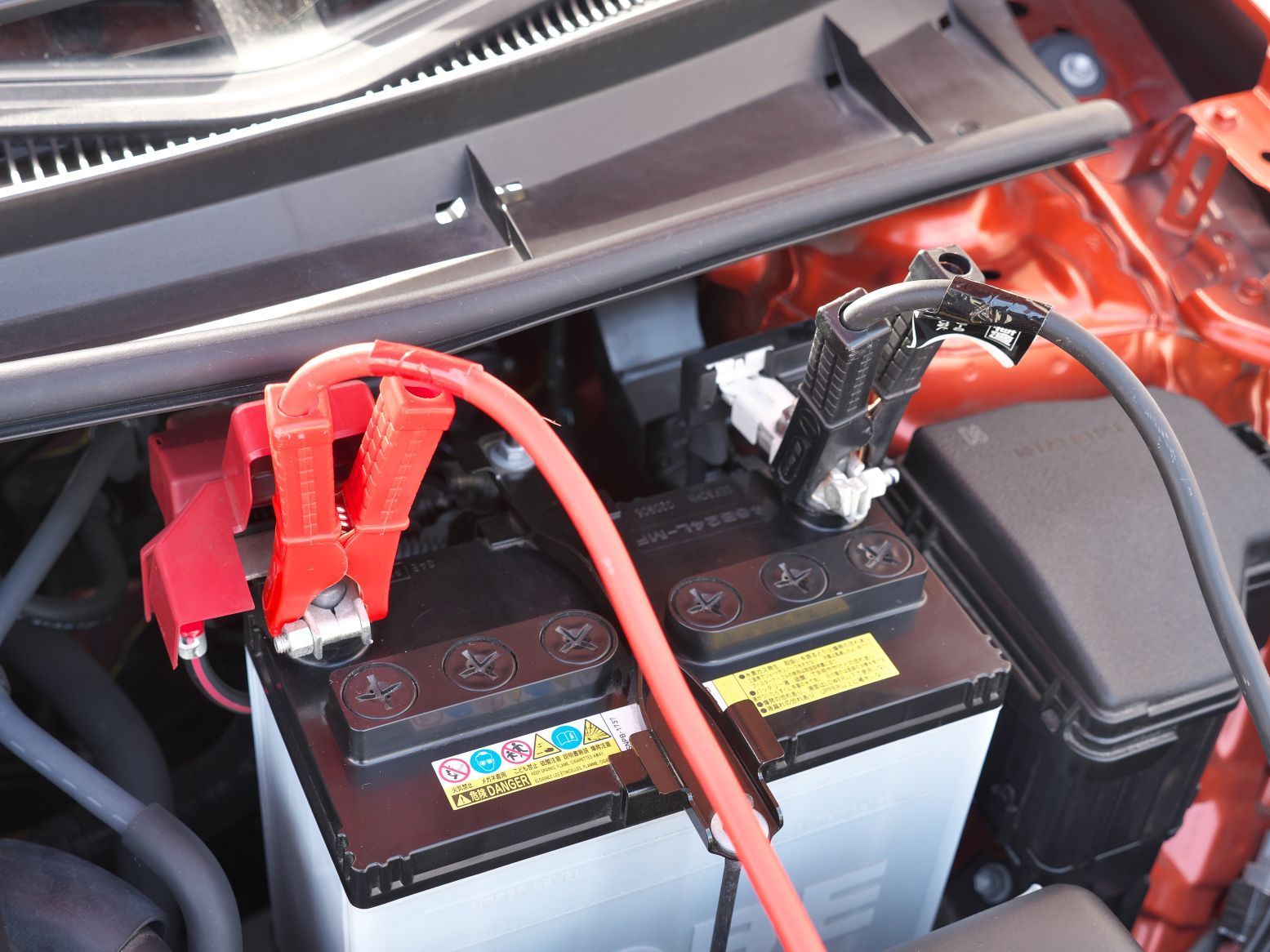 Car engine bay with two car batteries and red and black jumper cables connected in Fayetteville, NC.