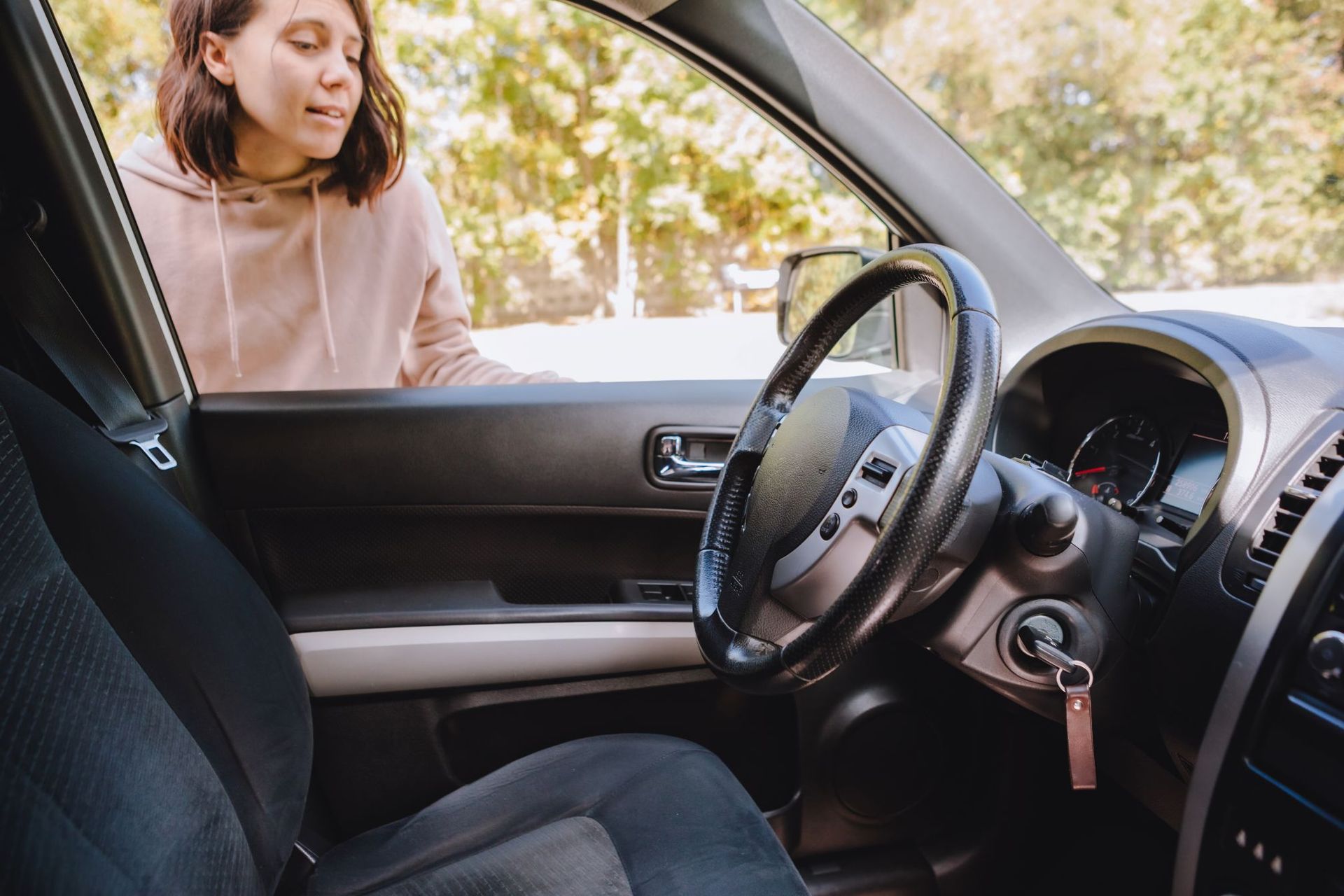 Woman leaning into a car through the open door, speaking to someone inside, with trees in the background in Fayetteville, NC.