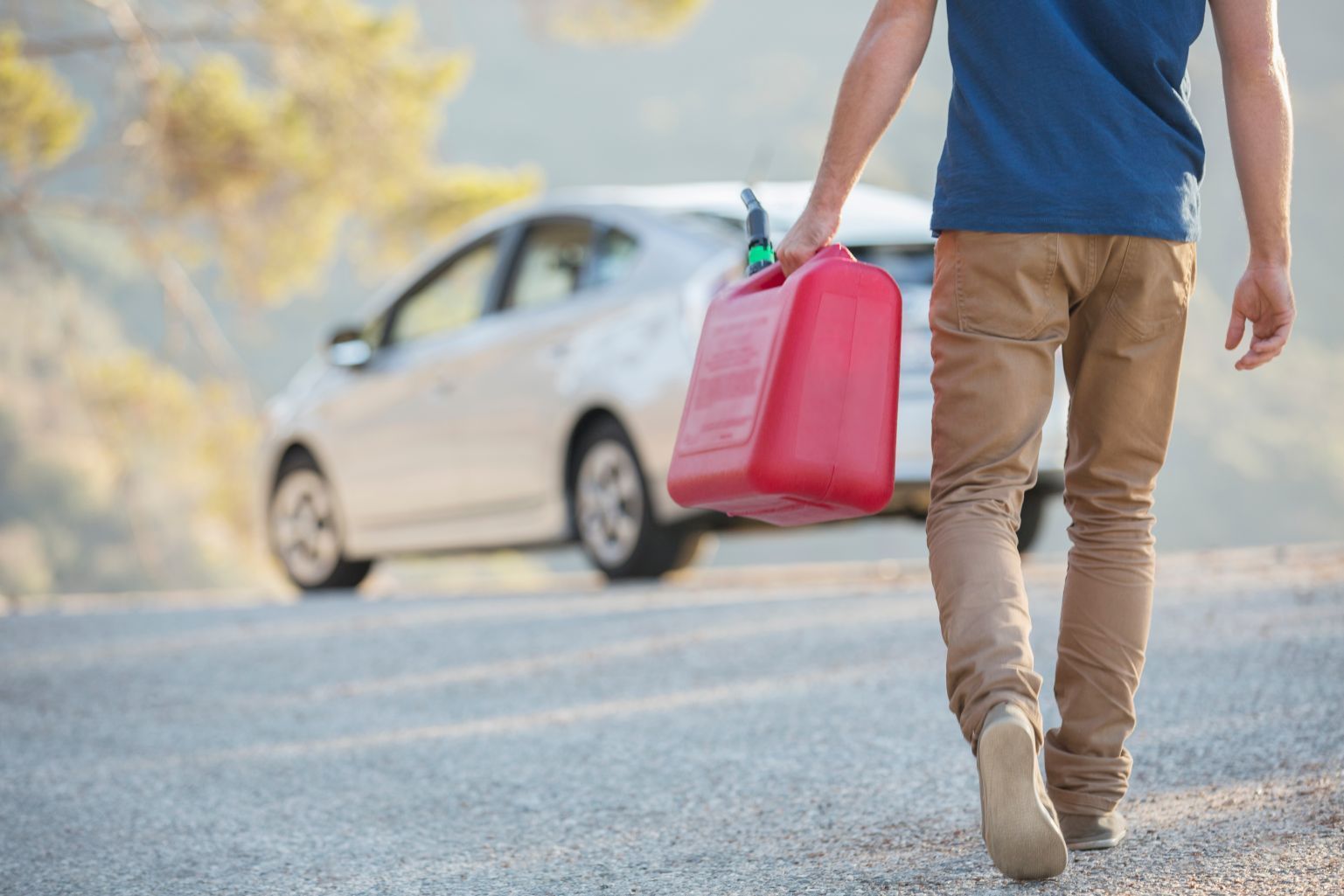 Person walking on roadside carrying a red fuel can toward a white car with its hood open in Fayetteville, NC.