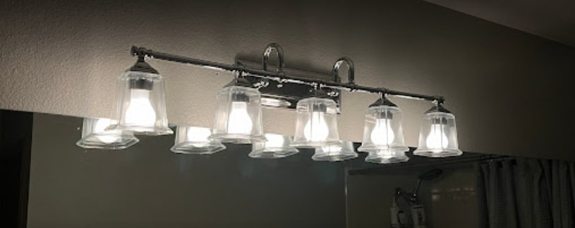 A bathroom vanity light is lit up in front of a mirror.