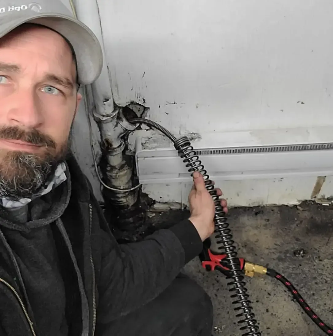 Un homme avec une barbe est à genoux et tient un tuyau.