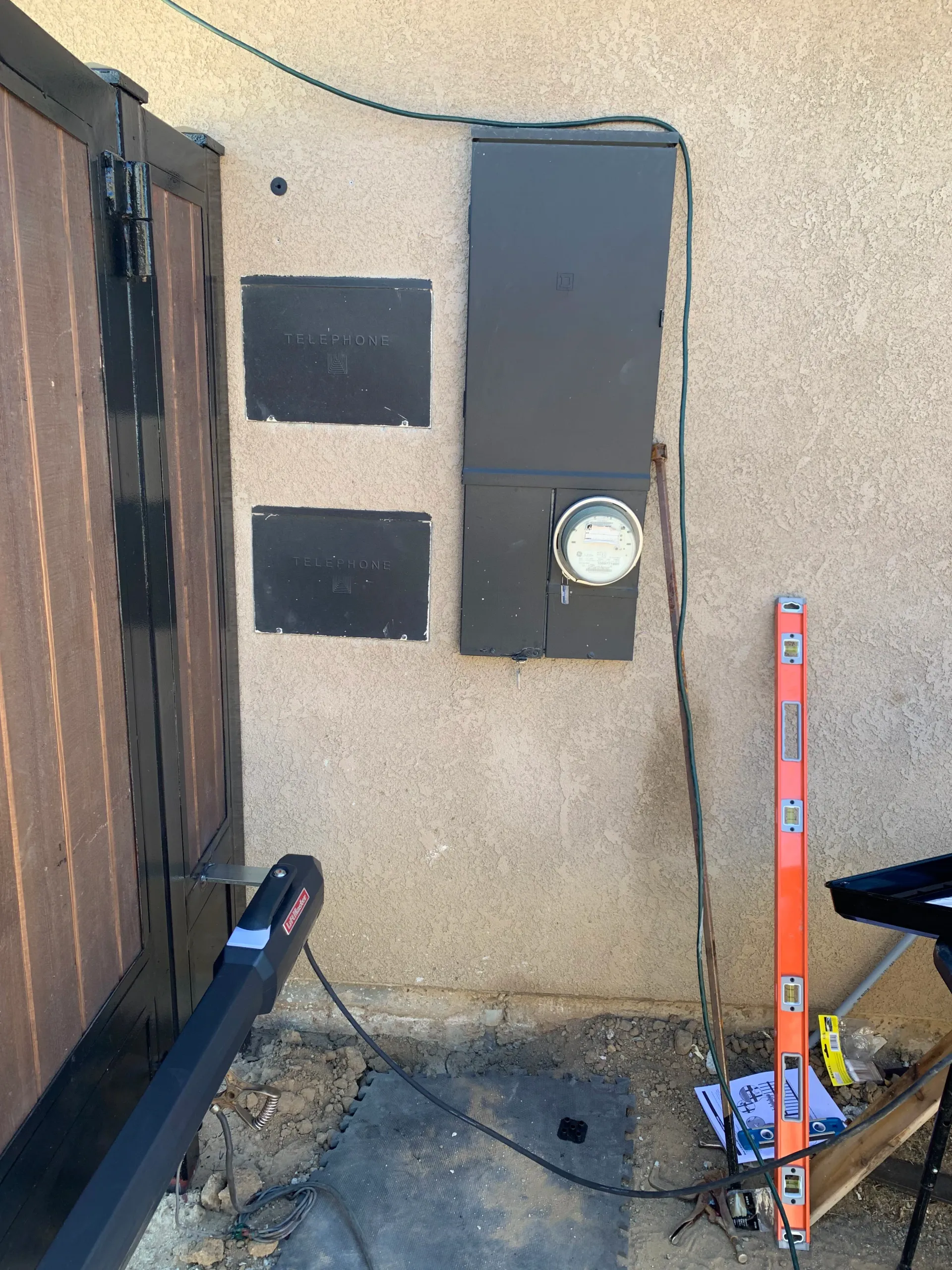 Outdoor wall with two black boxes, a gray electrical panel, and orange survey pole on a concrete slab in 93314 Bakersfield, CA