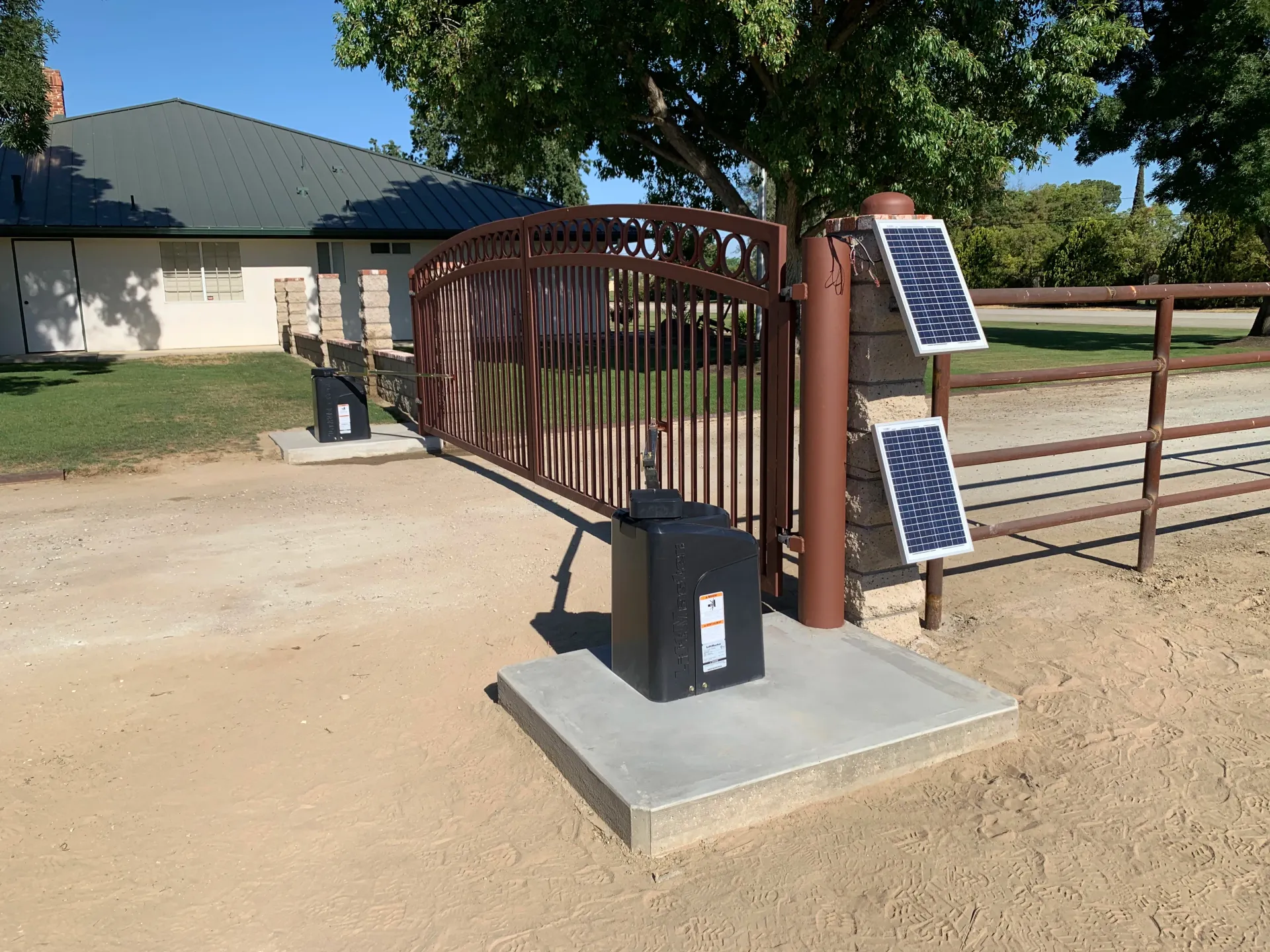 Solar-powered gate opener beside a brown metal driveway gate on a concrete pad.