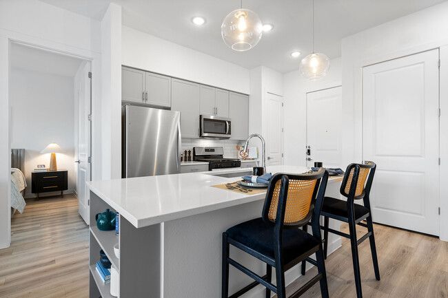 Modern white kitchen with stainless steel appliances, island seating, and light wood floors