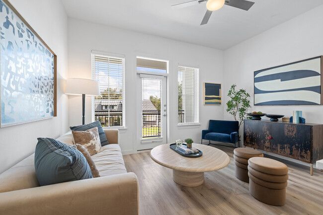 Bright modern living room with beige sofa, round coffee table, blue accents, and large windows