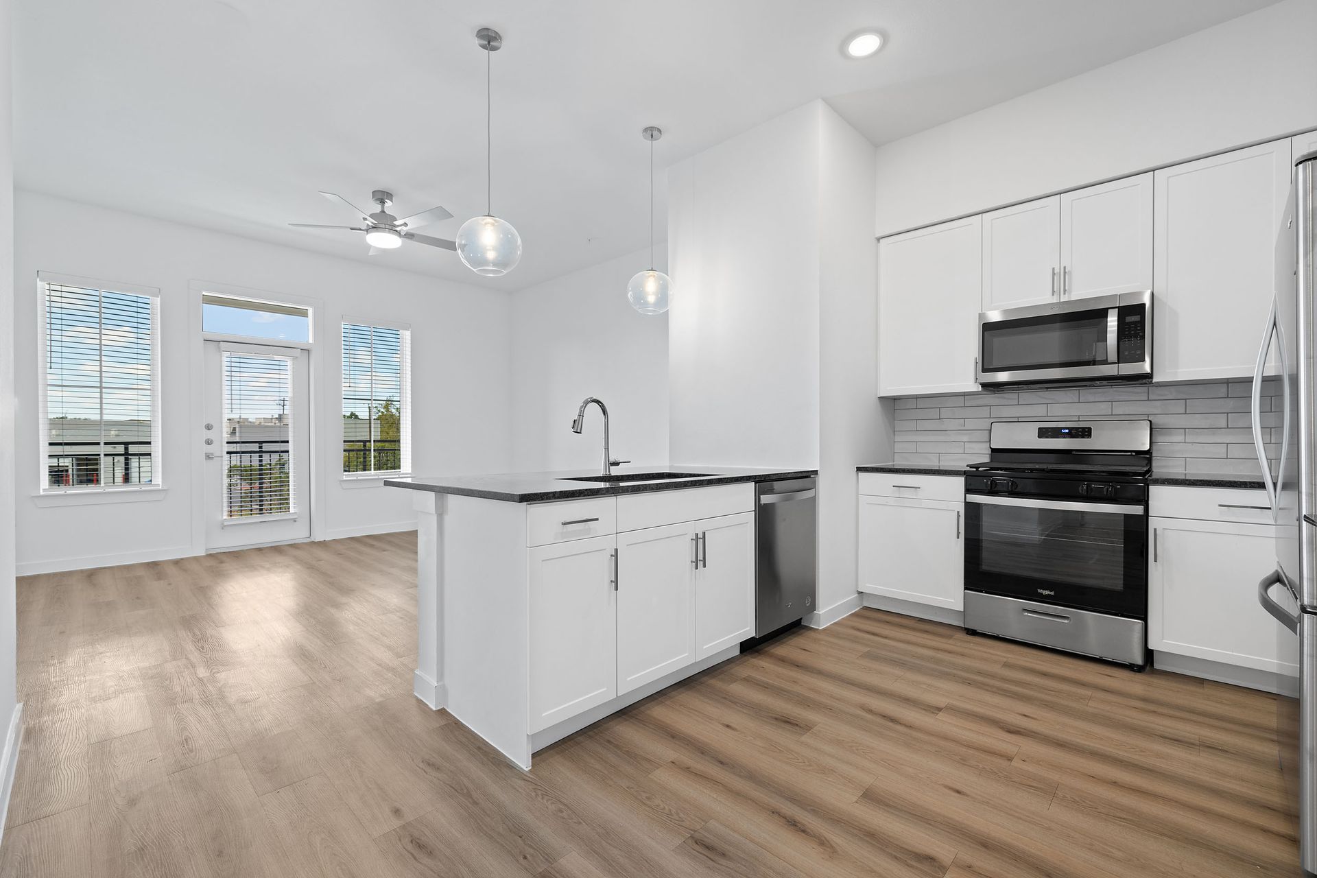 Open-concept apartment with  kitchen with white cabinets , stainless steel appliances , and hardwood floors overseeing the living room and balcony at The Everett, offering apartments for rent in Northwest Austin, TX.