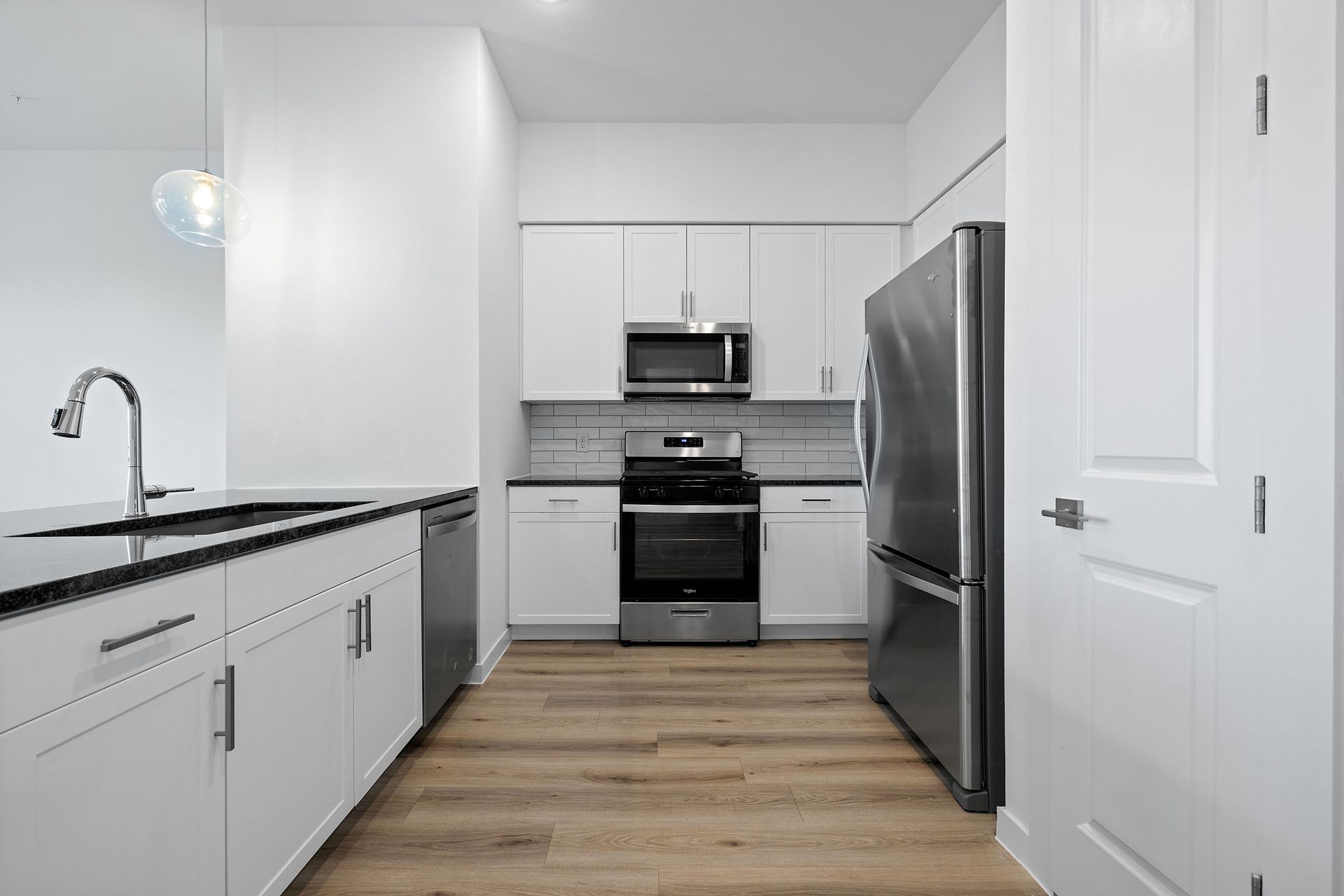 A chef-inspired kitchen with white cabinets, stainless steel appliances, a sink , an island, and a refrigerator at The Everett, offering apartments for rent in Northwest Austin, TX