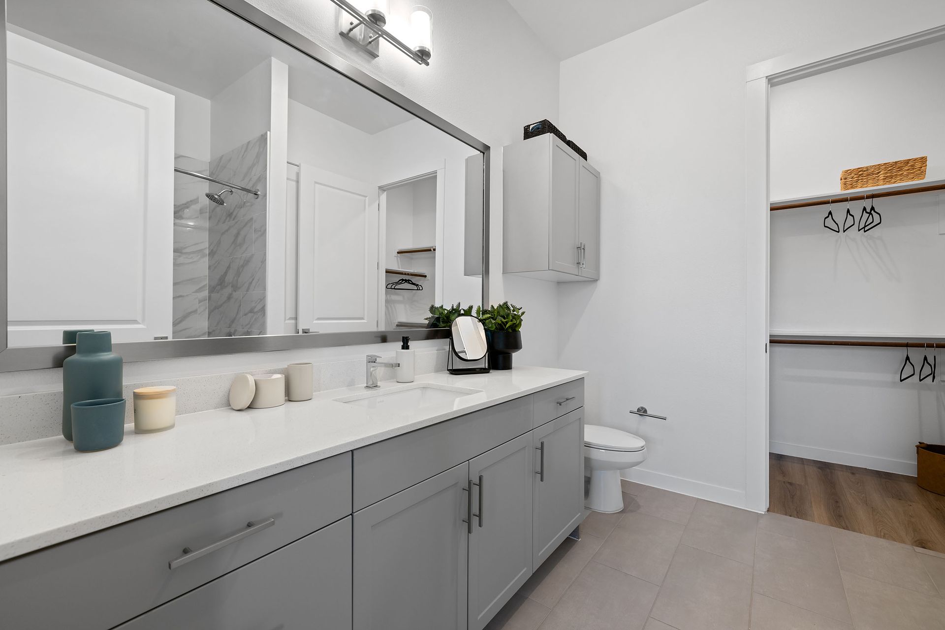 Modern bathroom with a sink, toilet, mirror, light grey cabinets, and walk in closet at The Everett, offering apartments for rent in Northwest Austin, TX