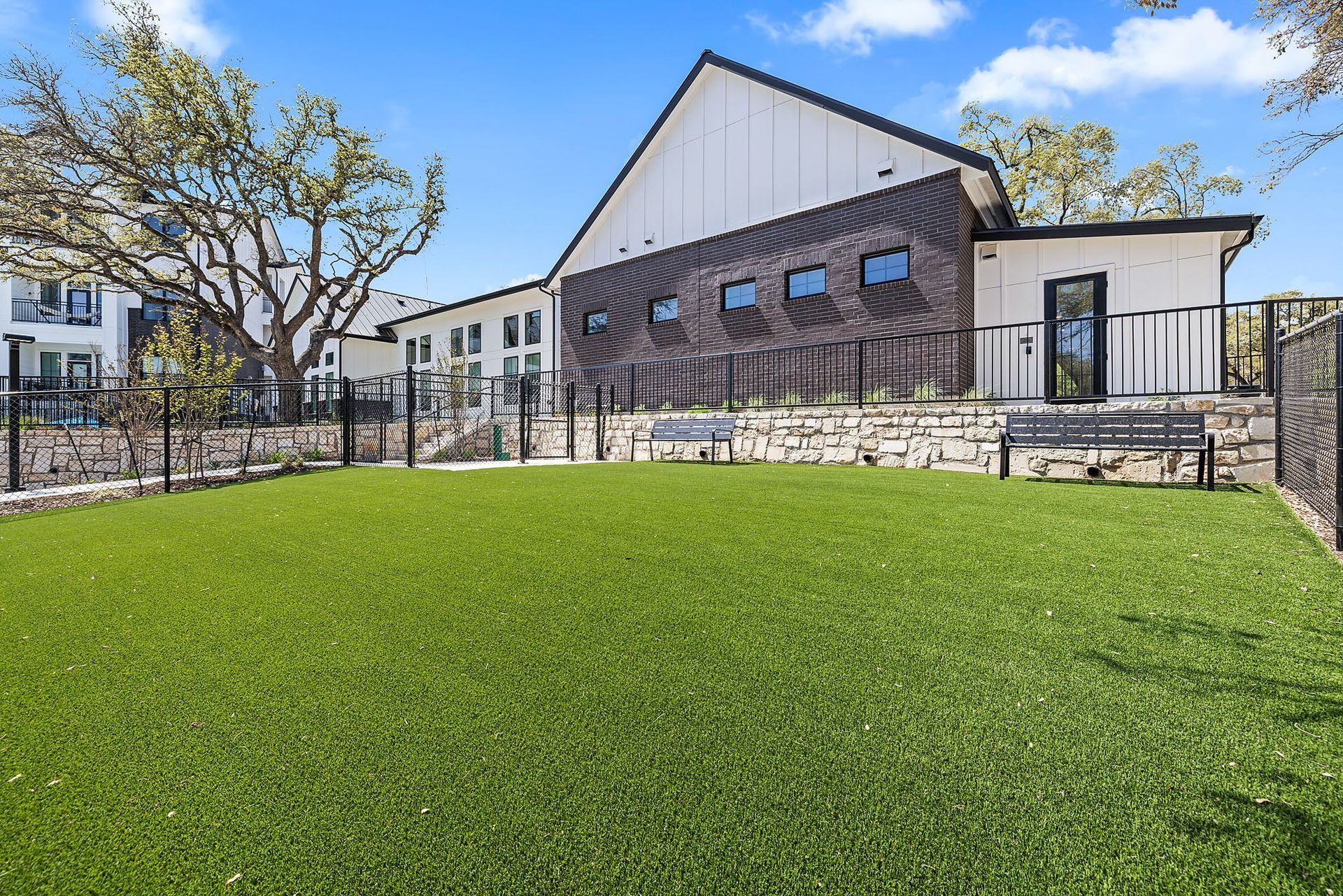 A large pet park with a spacious lawn in front of a building with a fence and a bench at The Everett, offering pet-friendly apartments in Austin, TX.