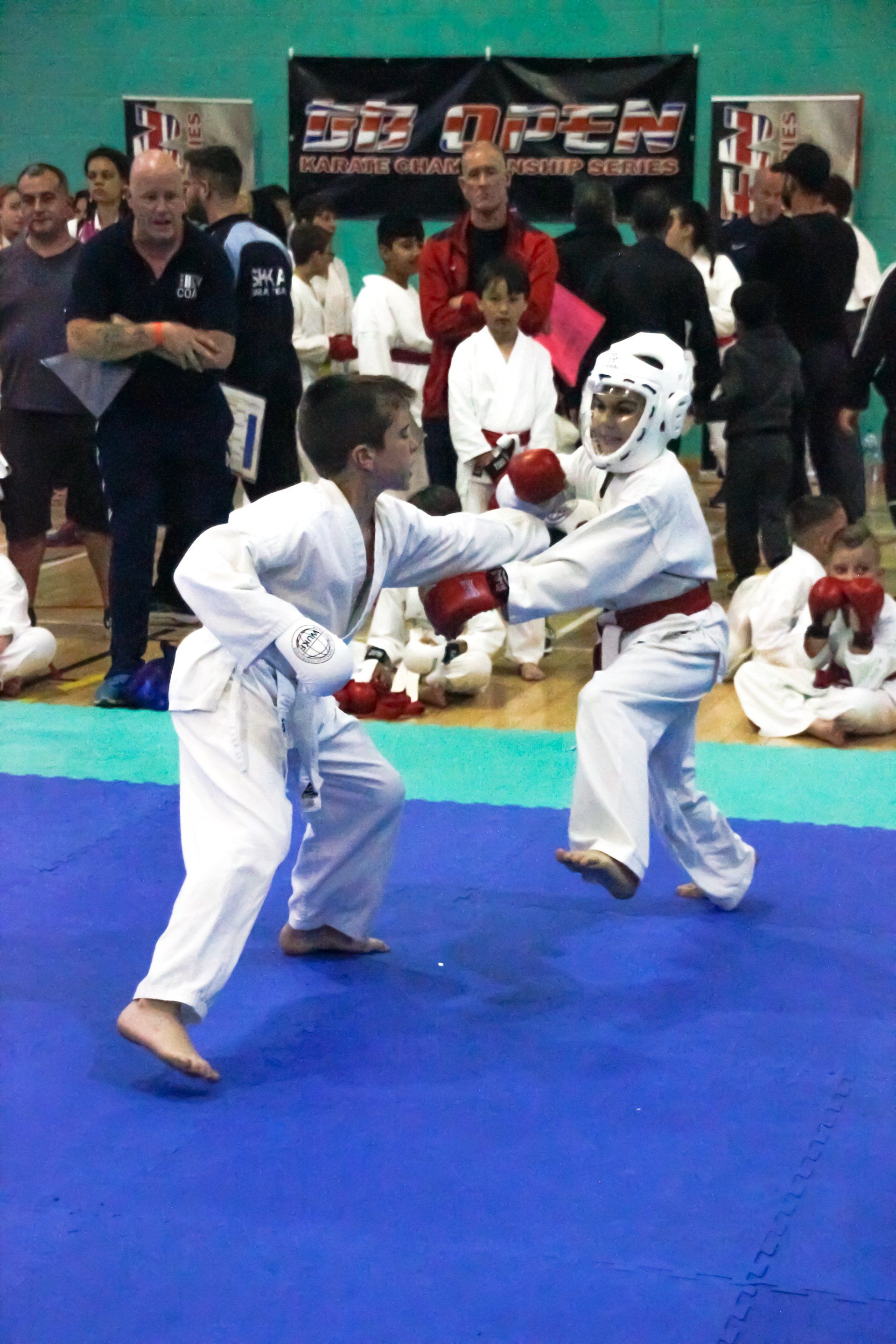 Two martial artists sparring on a blue mat at an indoor tournament