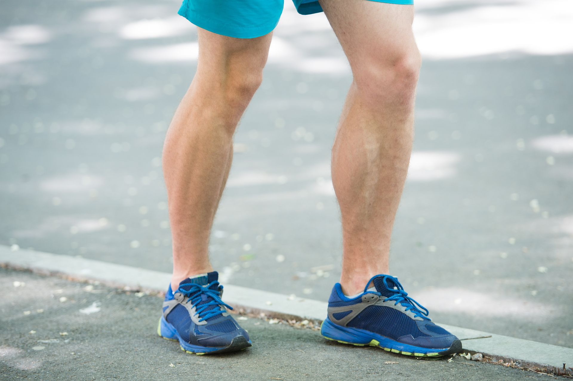Man's legs and feet in blue running shoes on a paved surface.