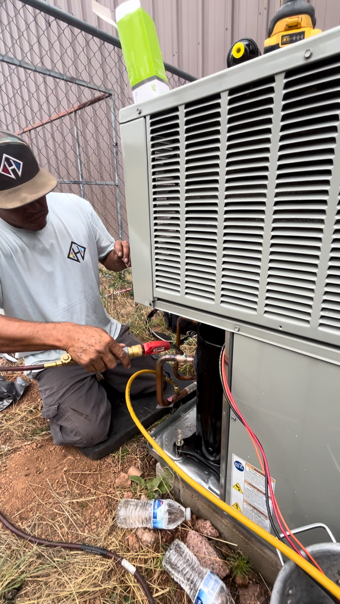 HVAC technician working on an air conditioning unit outside, using tools and connecting hoses.