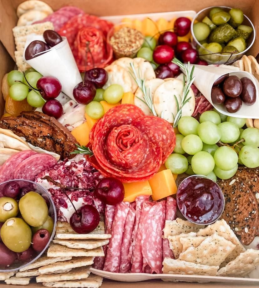 A box filled with lots of different types of food , including grapes , olives , crackers and meat.