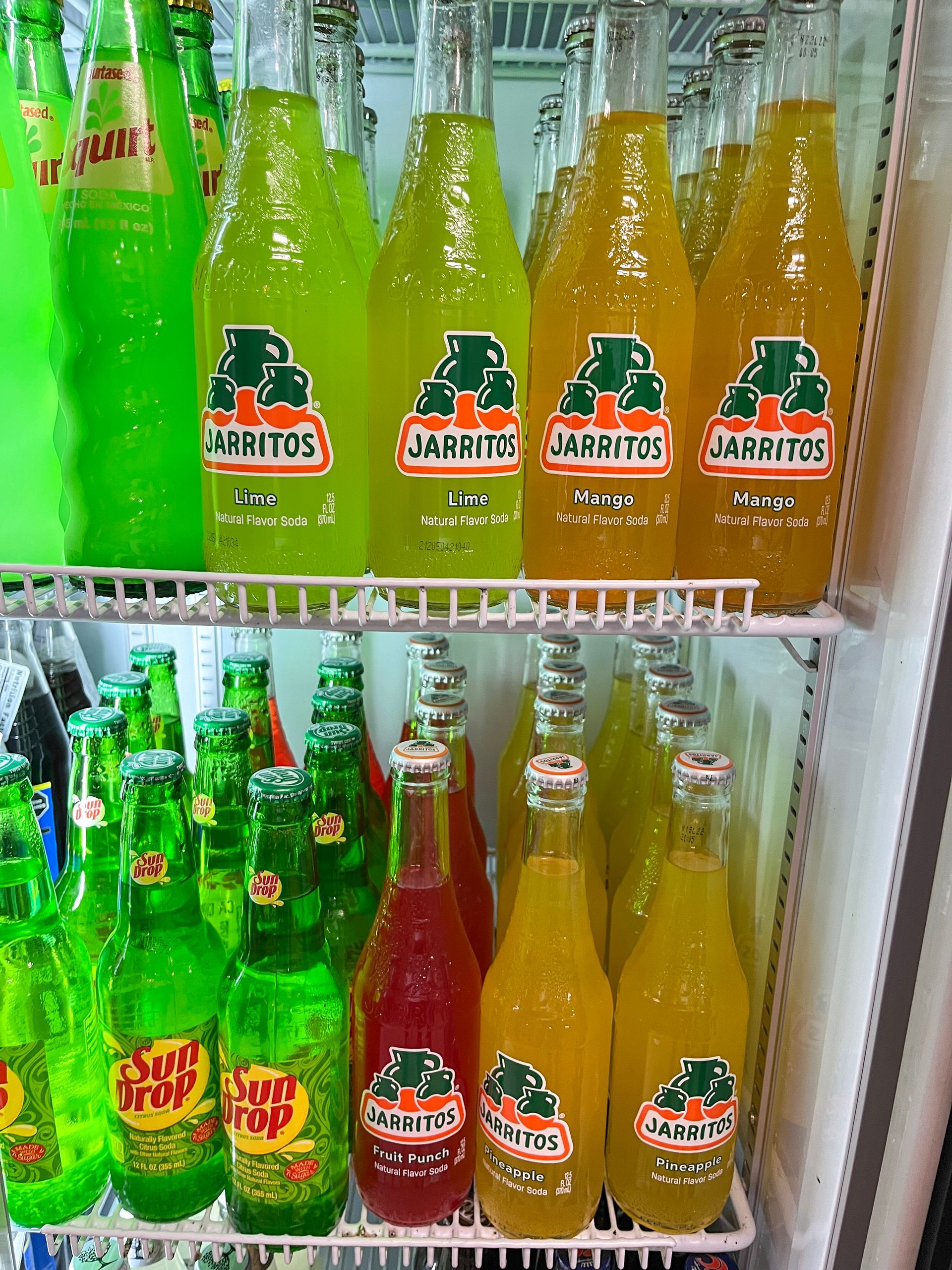 Colorful glass soda bottles on store shelves, including green, yellow, and orange drinks. Grasshopper Farms Knightdale, NC