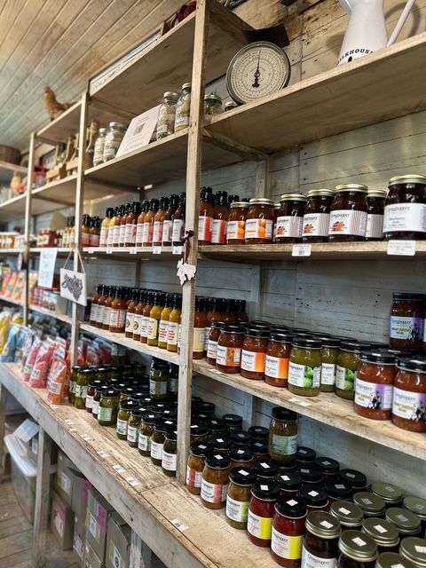 Shelves stocked with jars and bottles of assorted food products in a rustic store aisle. Grasshopper Farms Knightdale, NC