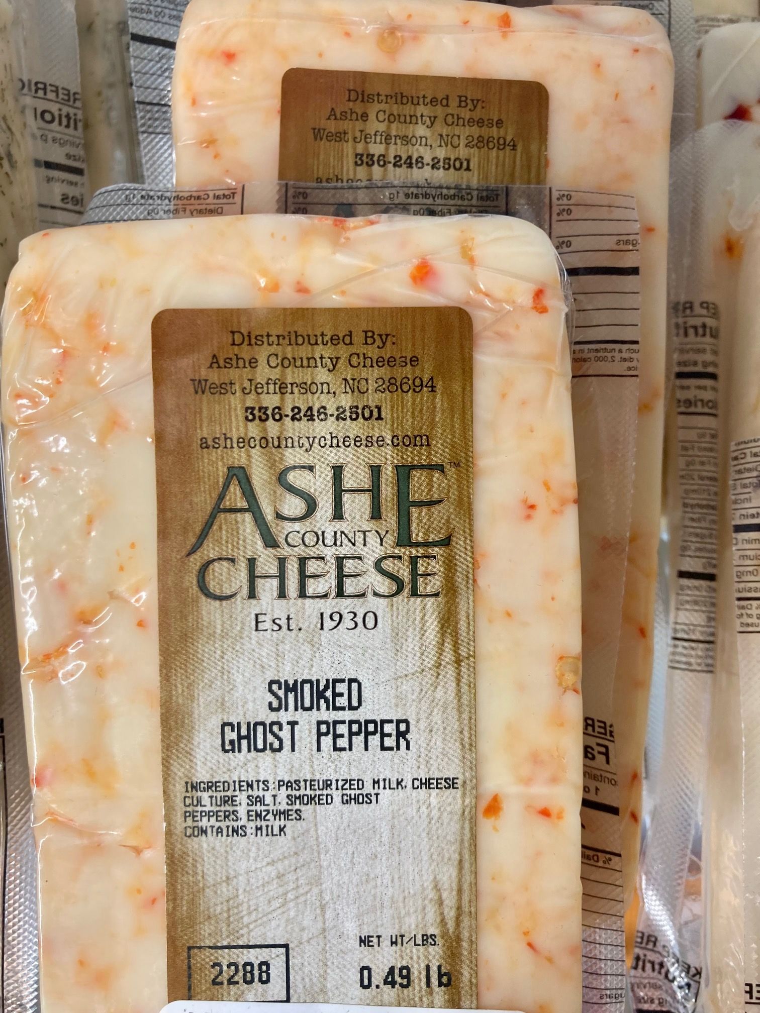 Two Ash Cheeese smoked ghost pepper cheese blocks in clear packaging on a shelf. Grasshopper Farms Knightdale, NC