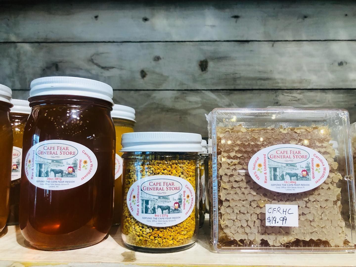 Jars and containers of honey and beeswax on a shelf against a wooden wall. Grasshopper Farms Knightdale, NC