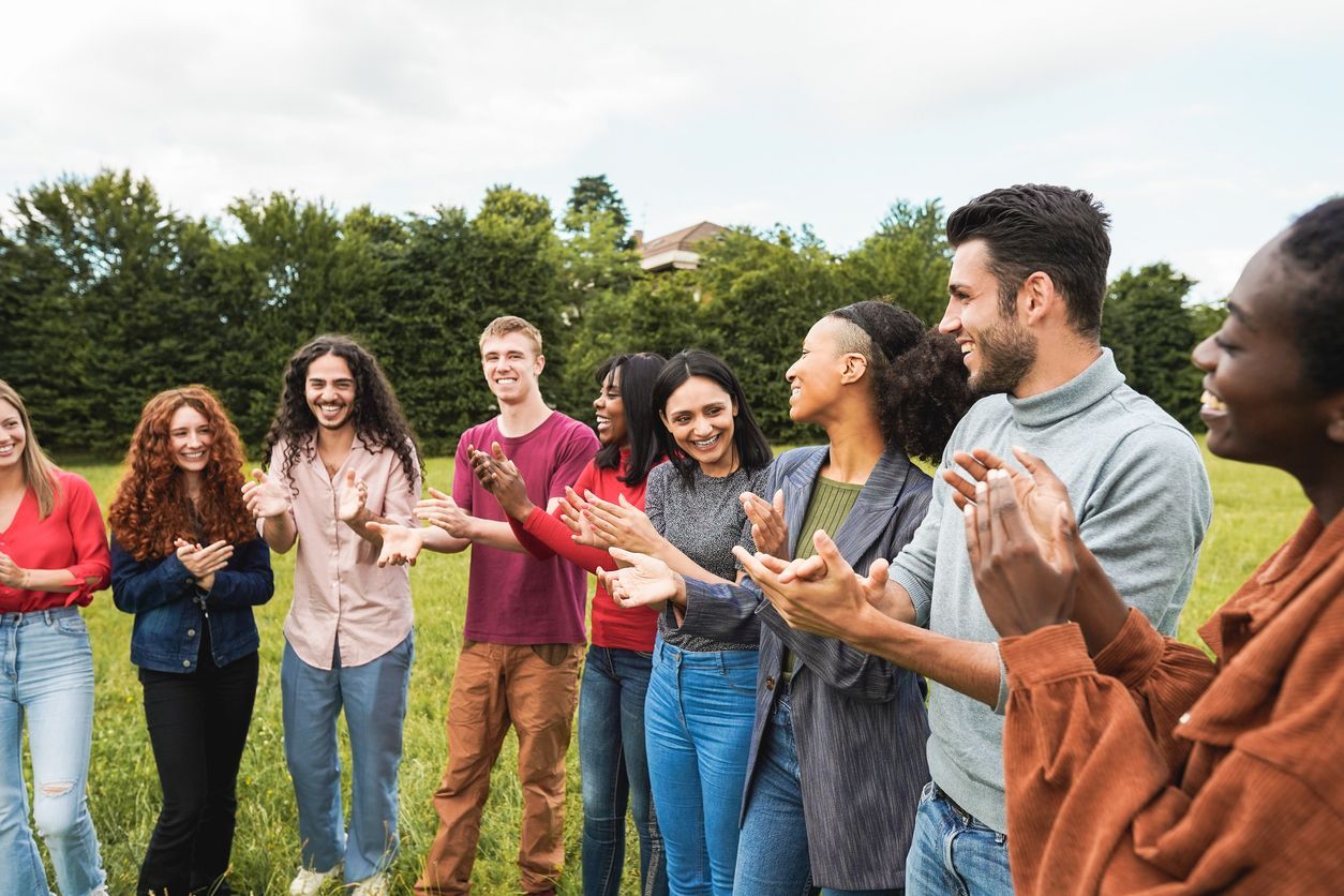 People clapping and smiling outdoors on a grassy field in a park. Grasshopper Farms Knightdale, NC