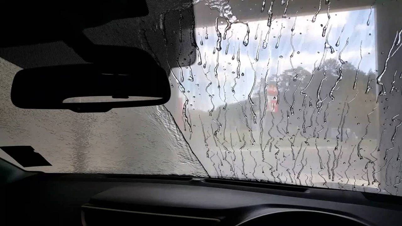 Regendruppels op de voorruit van de auto, wazig zicht op de weg.