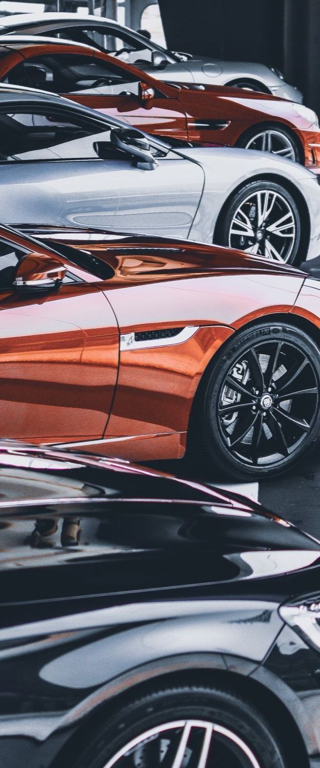 Een rij glanzende sportwagens in zwart, oranje en wit, geparkeerd in een autoshowroom.