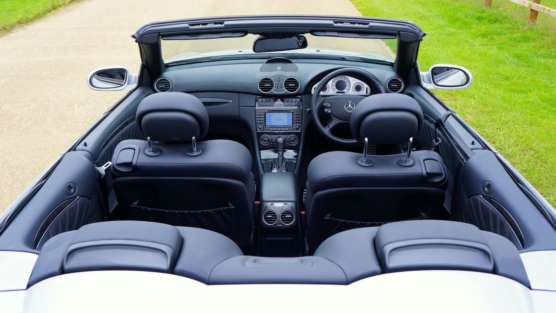 Het interieur van een zwarte cabriolet met vier zitplaatsen en het dak open, tegen een grasveld.