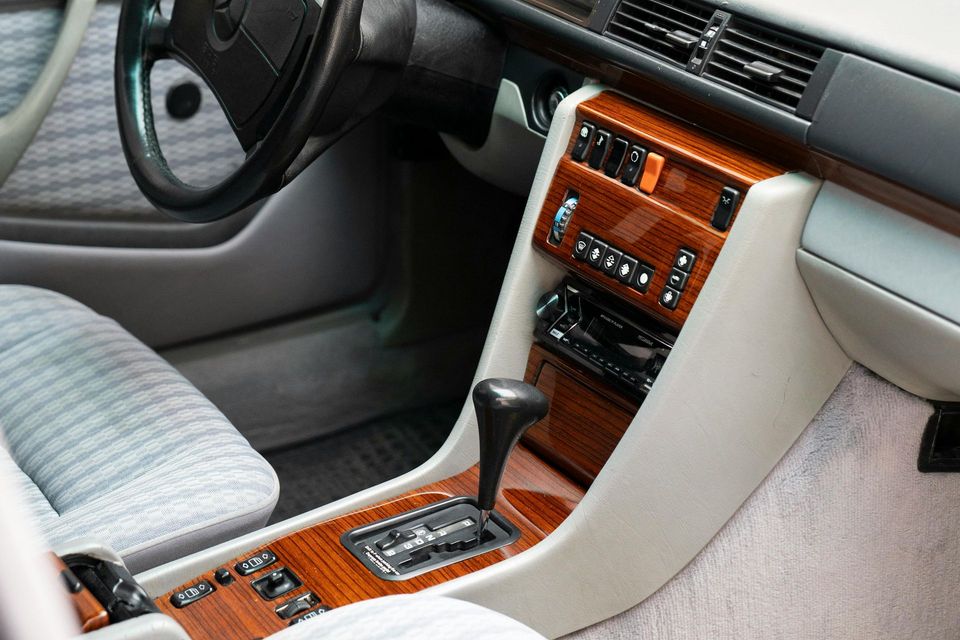 Auto-interieur met grijze stoelen, houten afwerking en een middenconsole met versnellingspook en bedieningselementen.