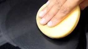 Hand die een gele spons vasthoudt op een zwart doek, maakt het oppervlak schoon.