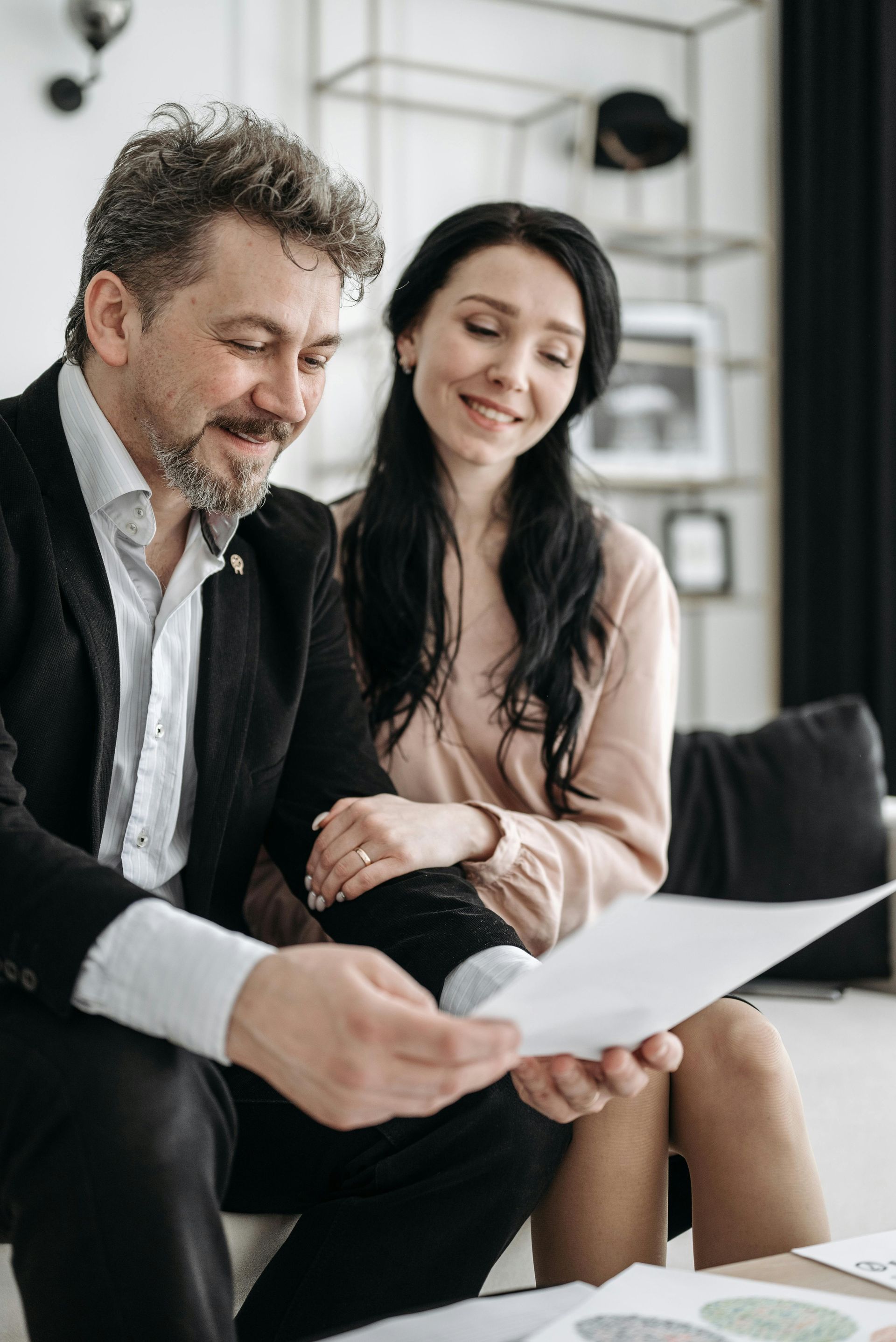 Man in suit and woman reviewing papers, both smiling, in a bright room.
