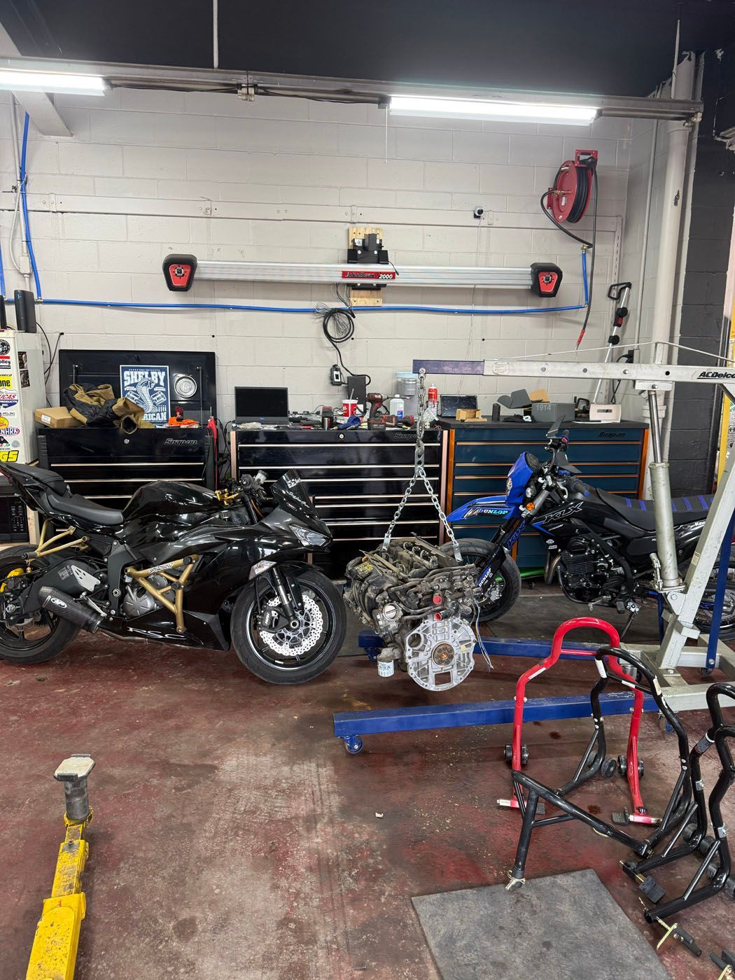 Motorcycle repair garage with two bikes, tools, and parts on a cluttered workshop floor