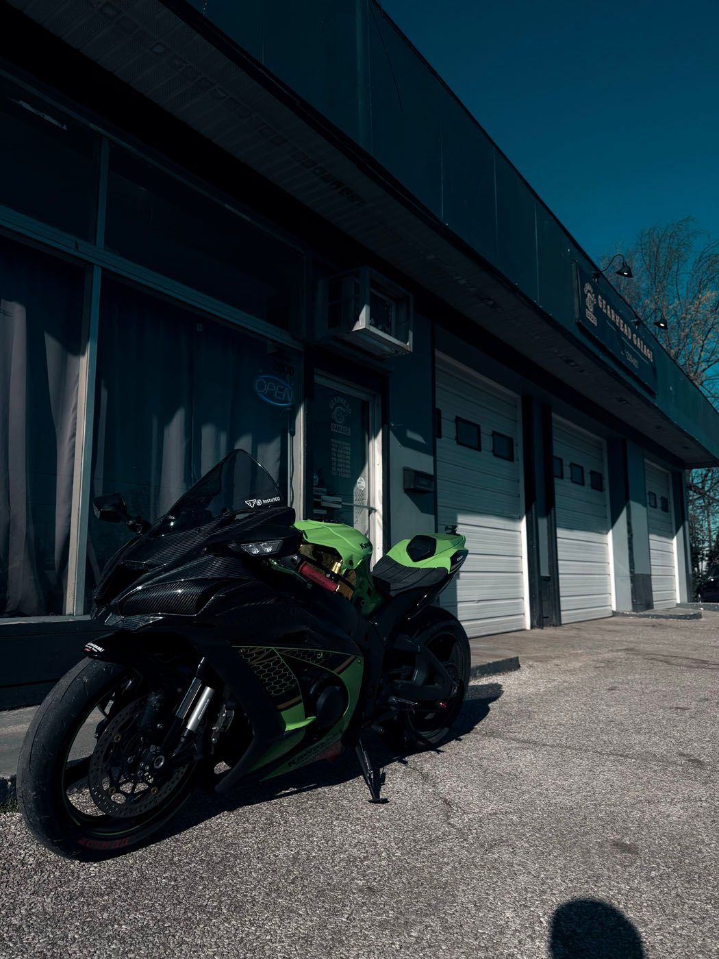Black and green sport motorcycle parked outside a building with garage doors and windows in sunlight