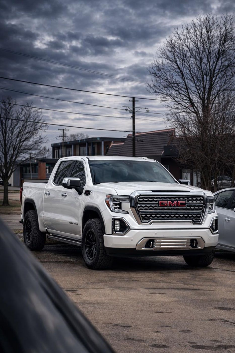White GMC pickup truck parked on a street under a cloudy sky, with bare trees in the background