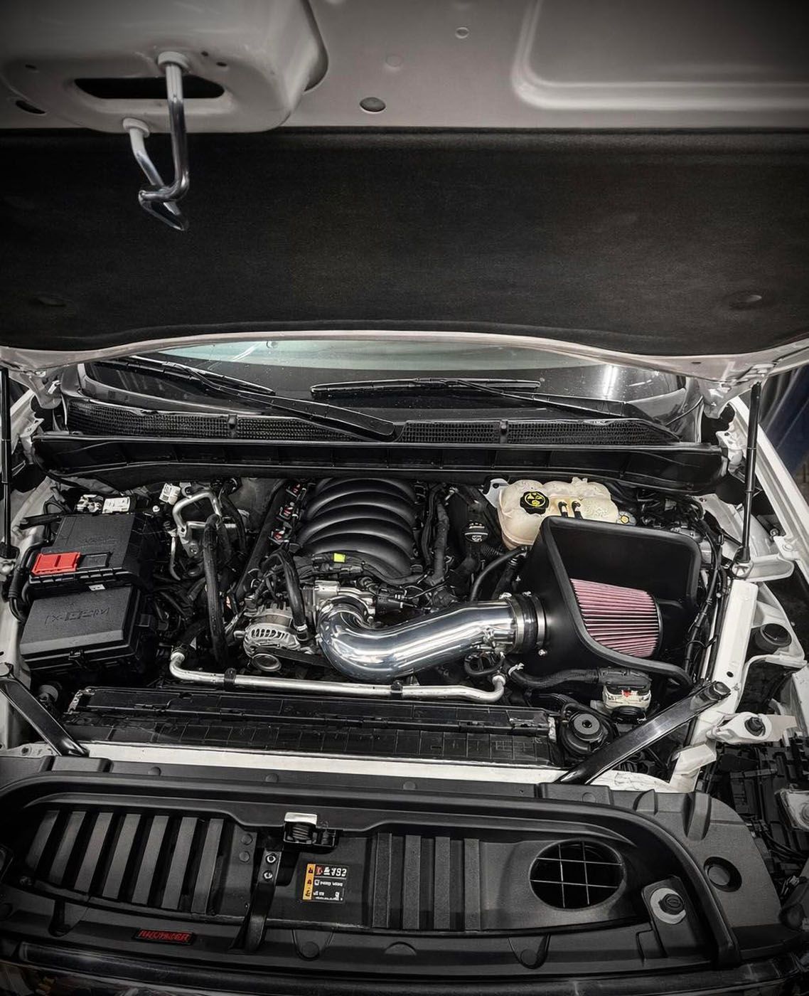 Car engine bay with a polished intake pipe and visible pink air filter under the hood