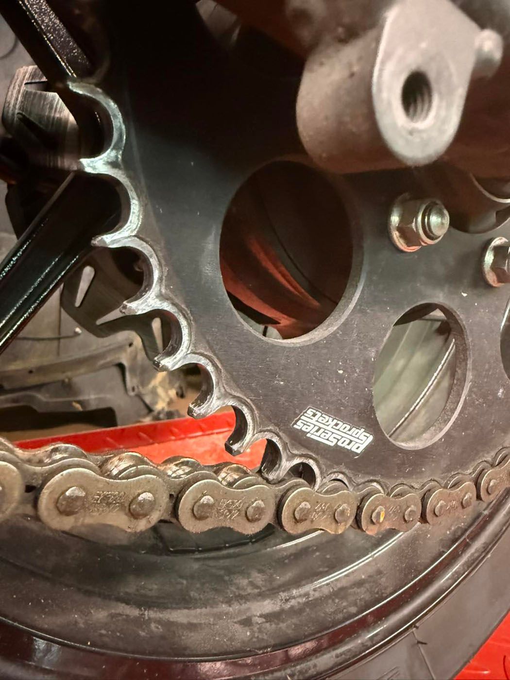 Close-up of a motorcycle chain and sprocket with red paint and a black wheel rim