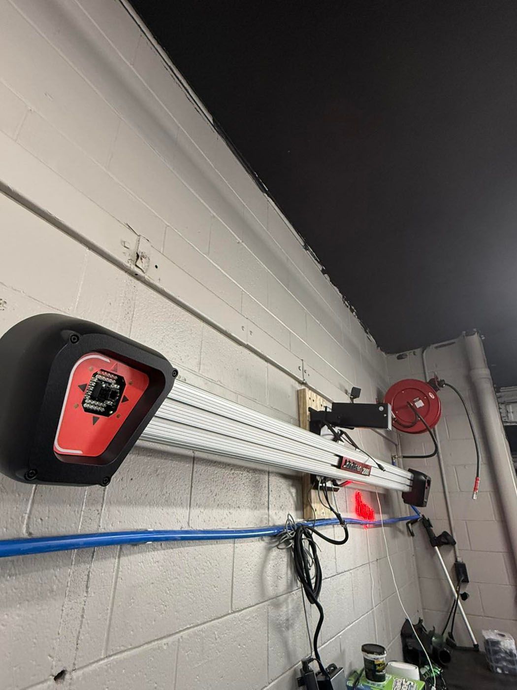 Garage wall with wall-mounted garage door opener, rail, and blue cable against a white block wall.