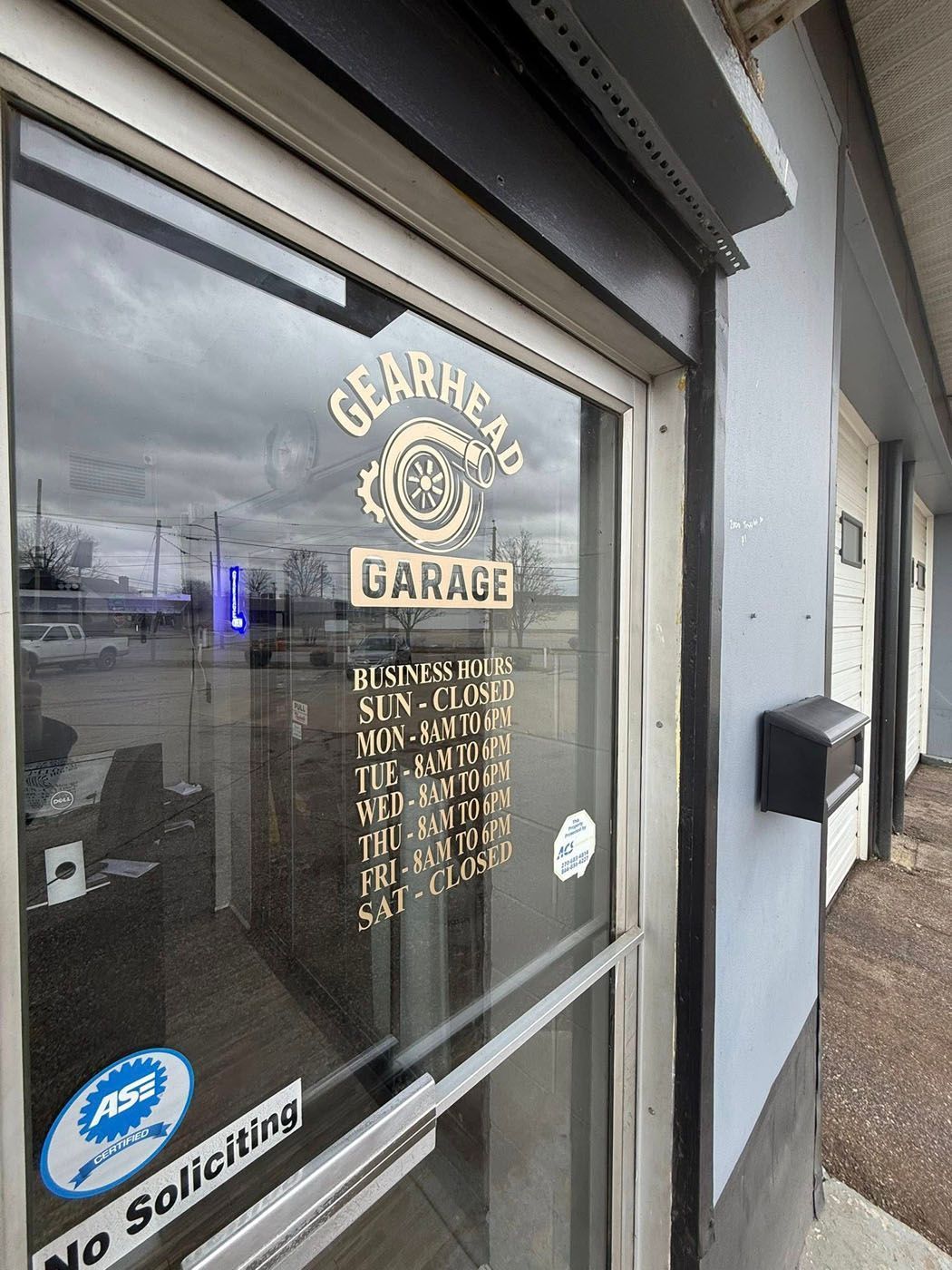 Glass storefront for “Gearhead Garage” with hours listed and a blue “No Soliciting” sign.
