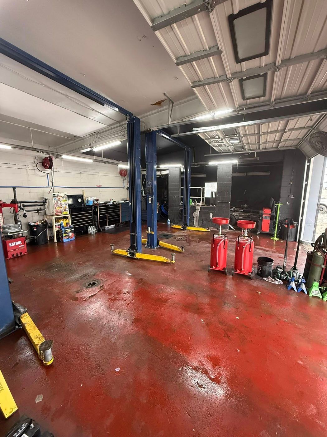 Auto repair shop interior with car lifts, tools, and a wet red floor