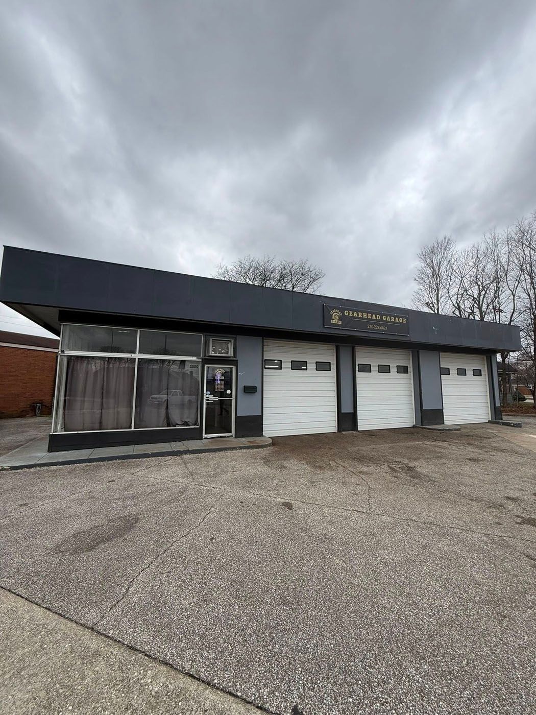 Commercial building with three white garage doors and a dark facade under a cloudy sky
