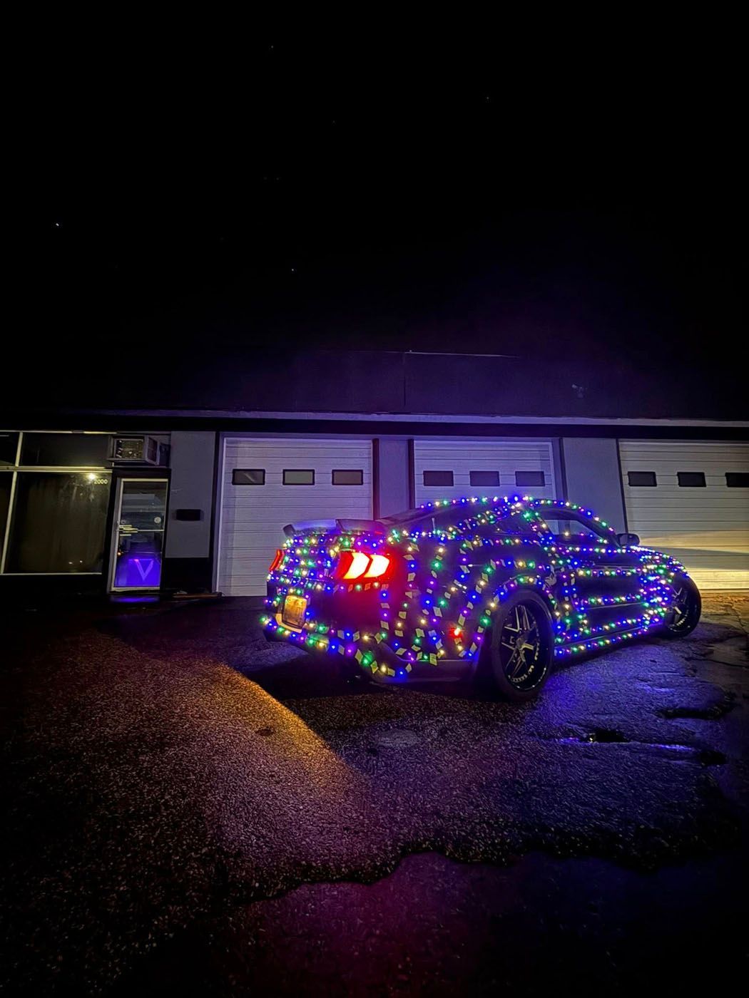 SUV covered in colorful holiday lights parked in front of a garage at night