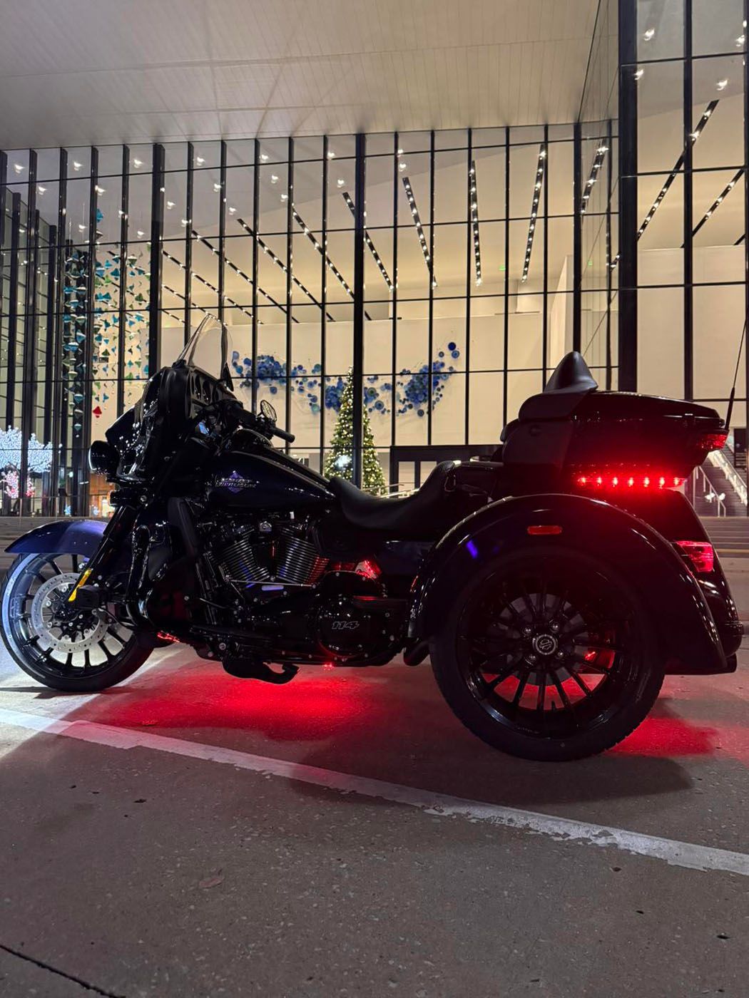 Black motorcycle with red underglow parked at night outside a modern building