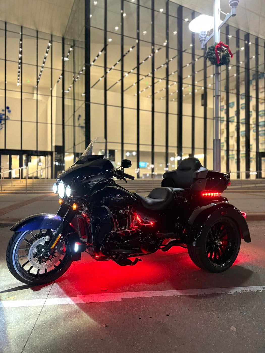 Black three-wheeled motorcycle with red underglow parked at night in front of a lit building